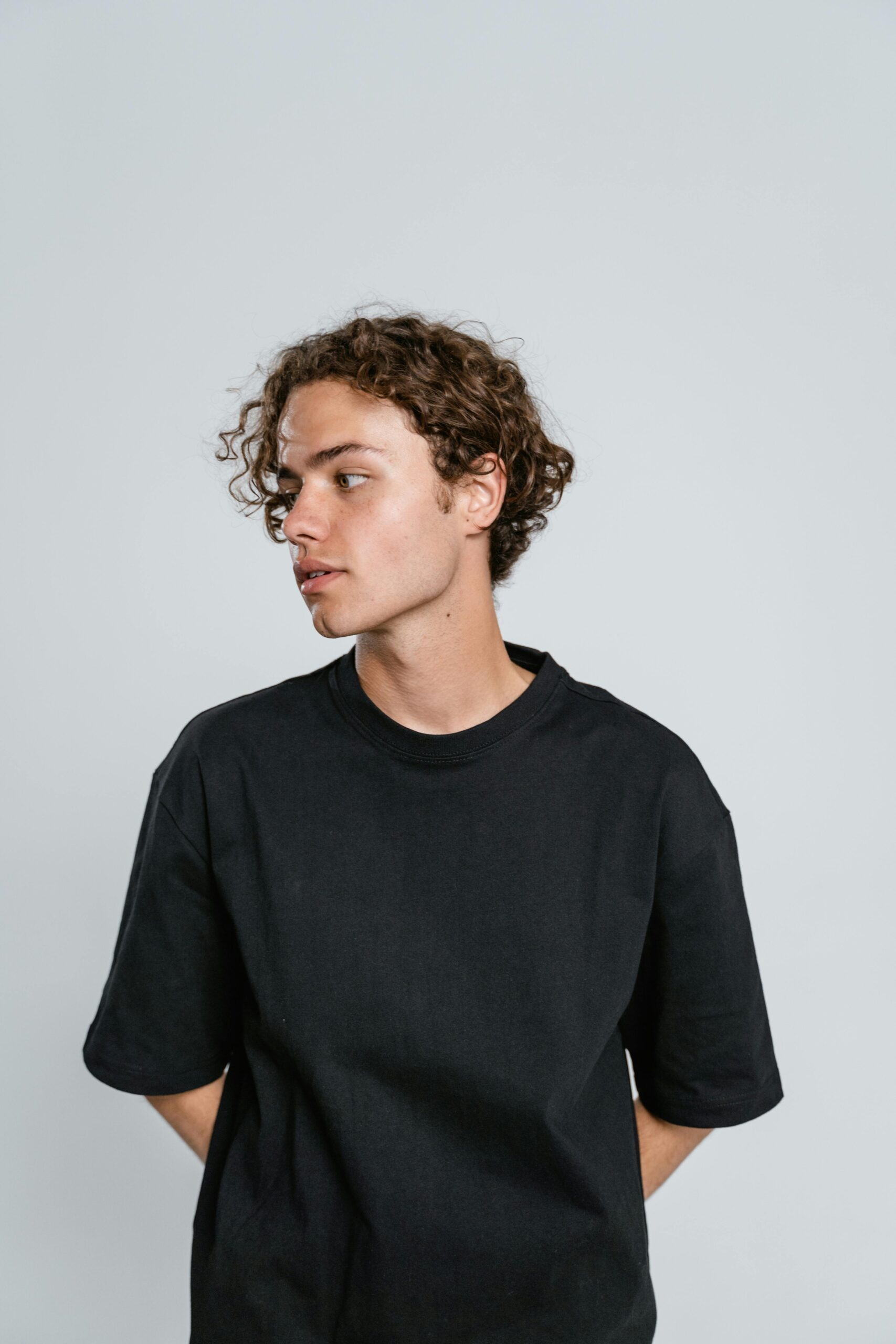 Portrait of a young man in a black t-shirt looking to the side, set against a neutral background.